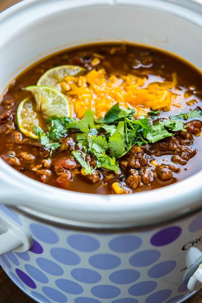 taco soup with cheese, lime wedges and cilantro in polka dot slow cooker