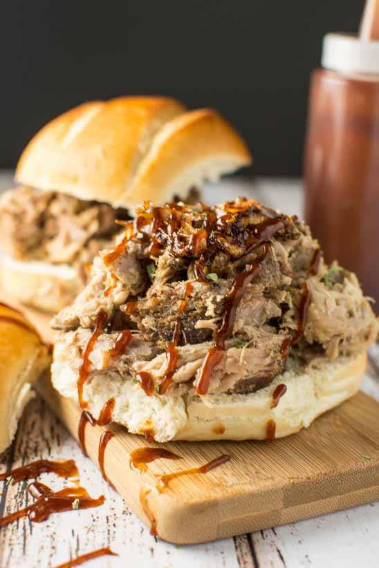 pulled pork on bun with bbq sauce drizzled over on wood cutting board with bbq sauce bottle in background