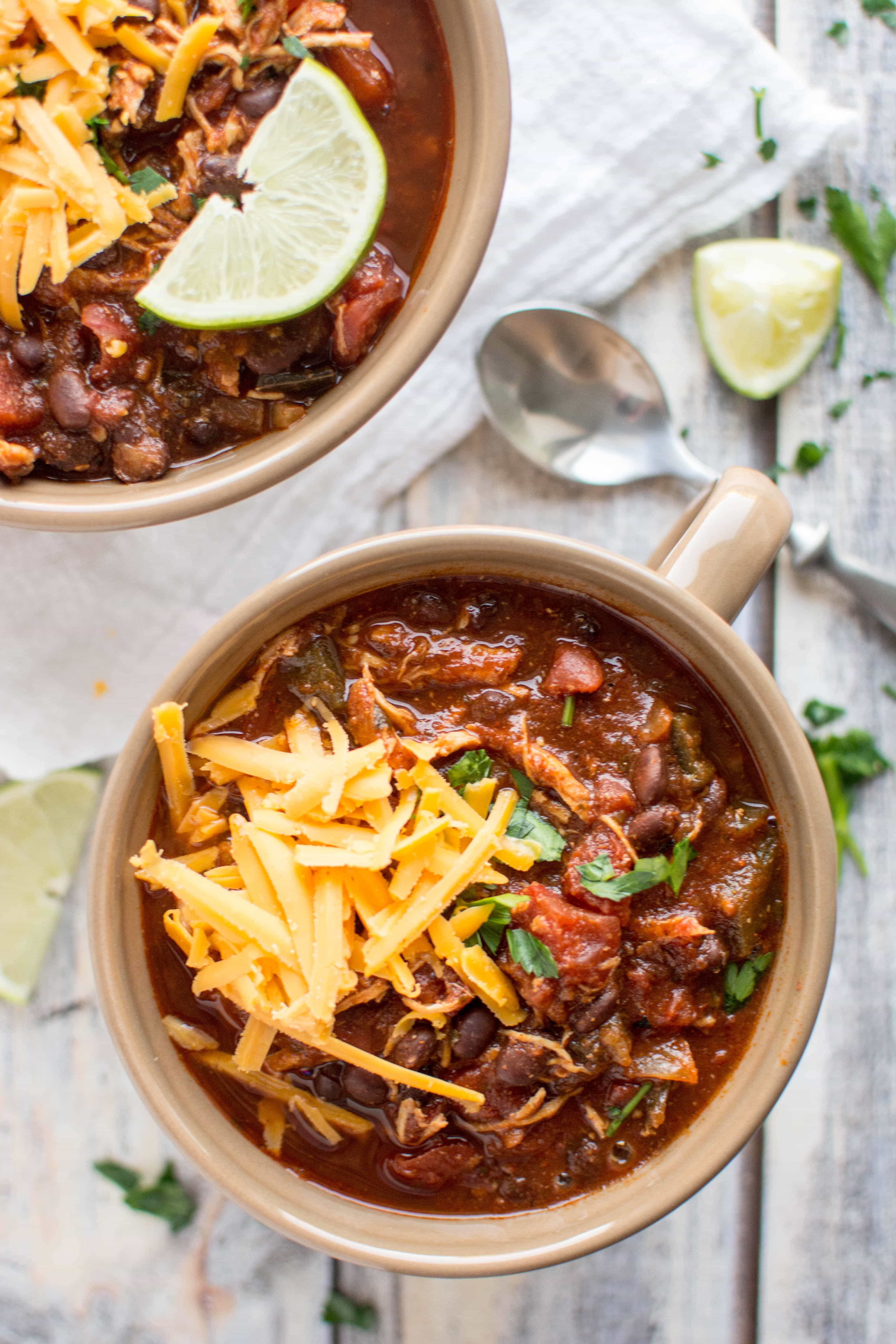 roasted tomato and ancho chicken chili in two tan serving bowls with cheese and lime wedge