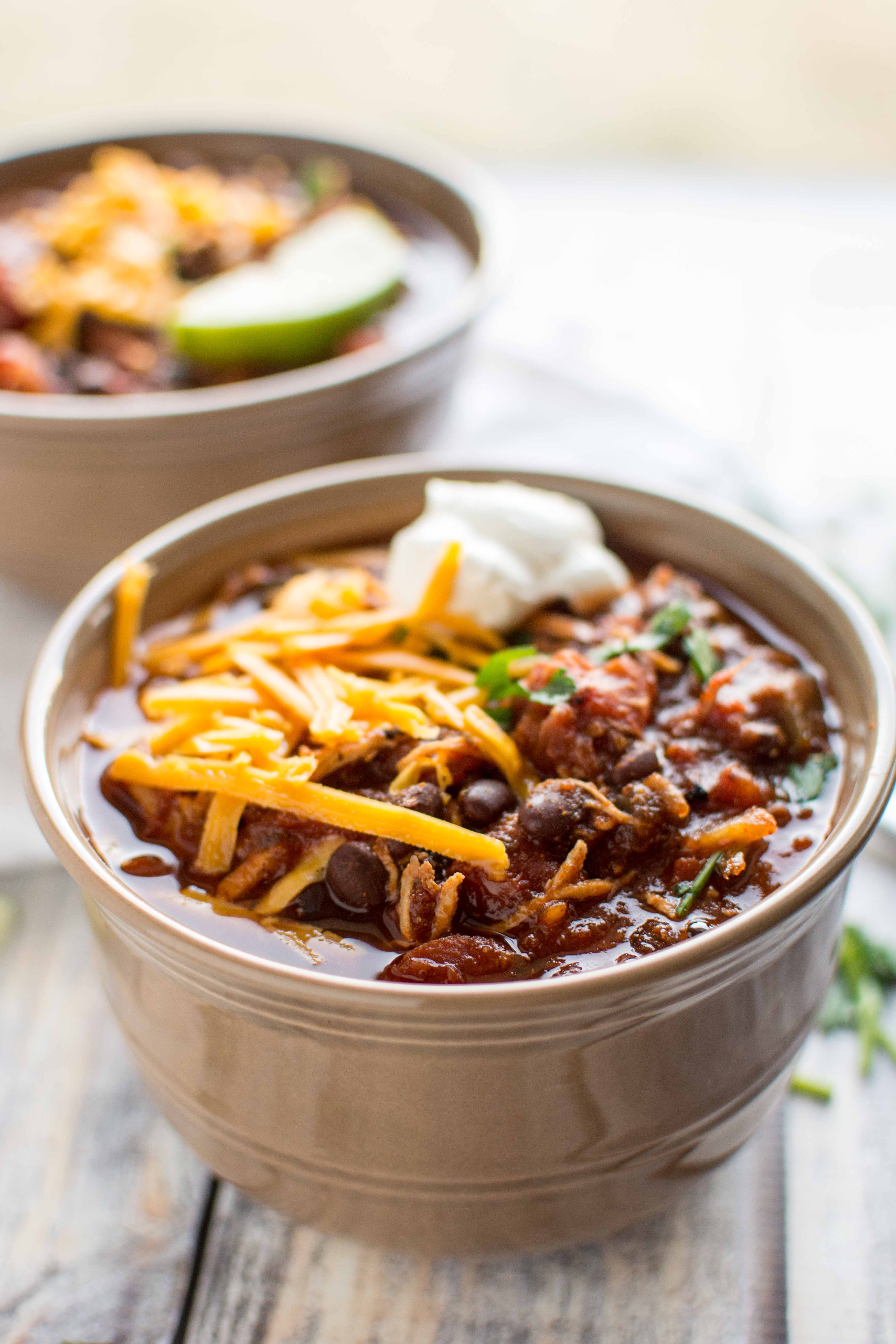 roasted tomato and ancho chicken chili in two tan serving bowls with cheese and sour cream