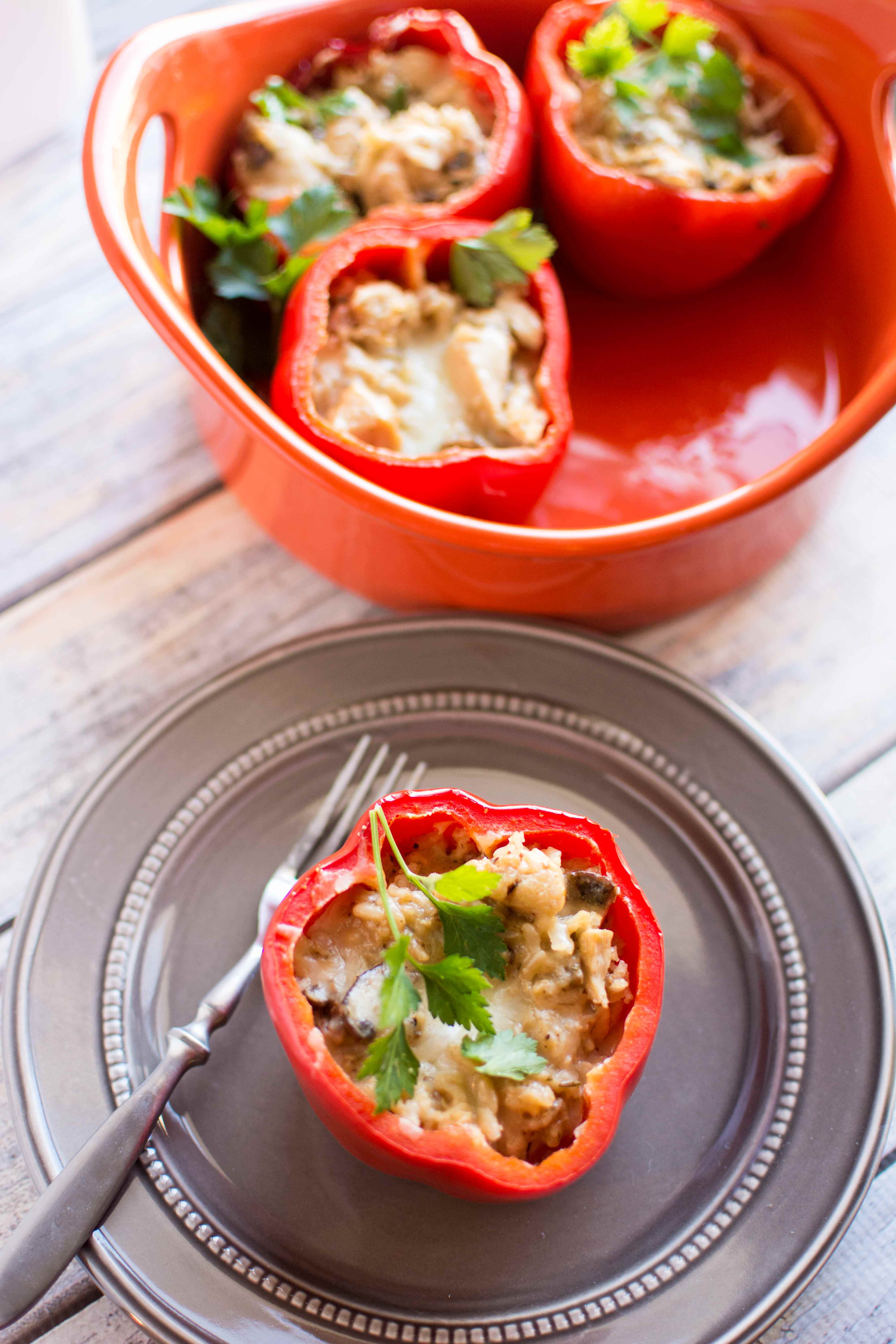 gray plate with one stuffed pepper with fork on side, with three stuffed red peppers in red serving dish in background