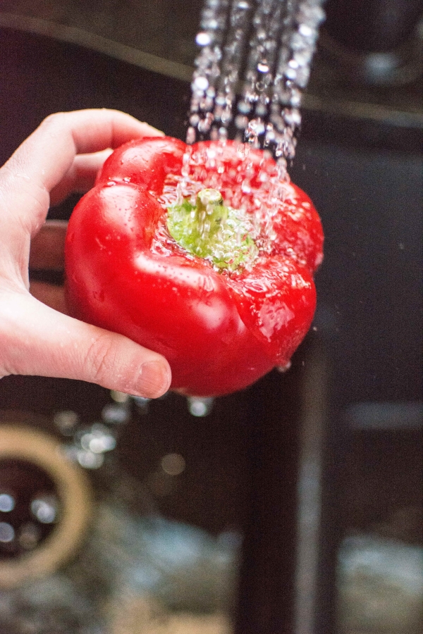 one red pepper under faucet with running tap water