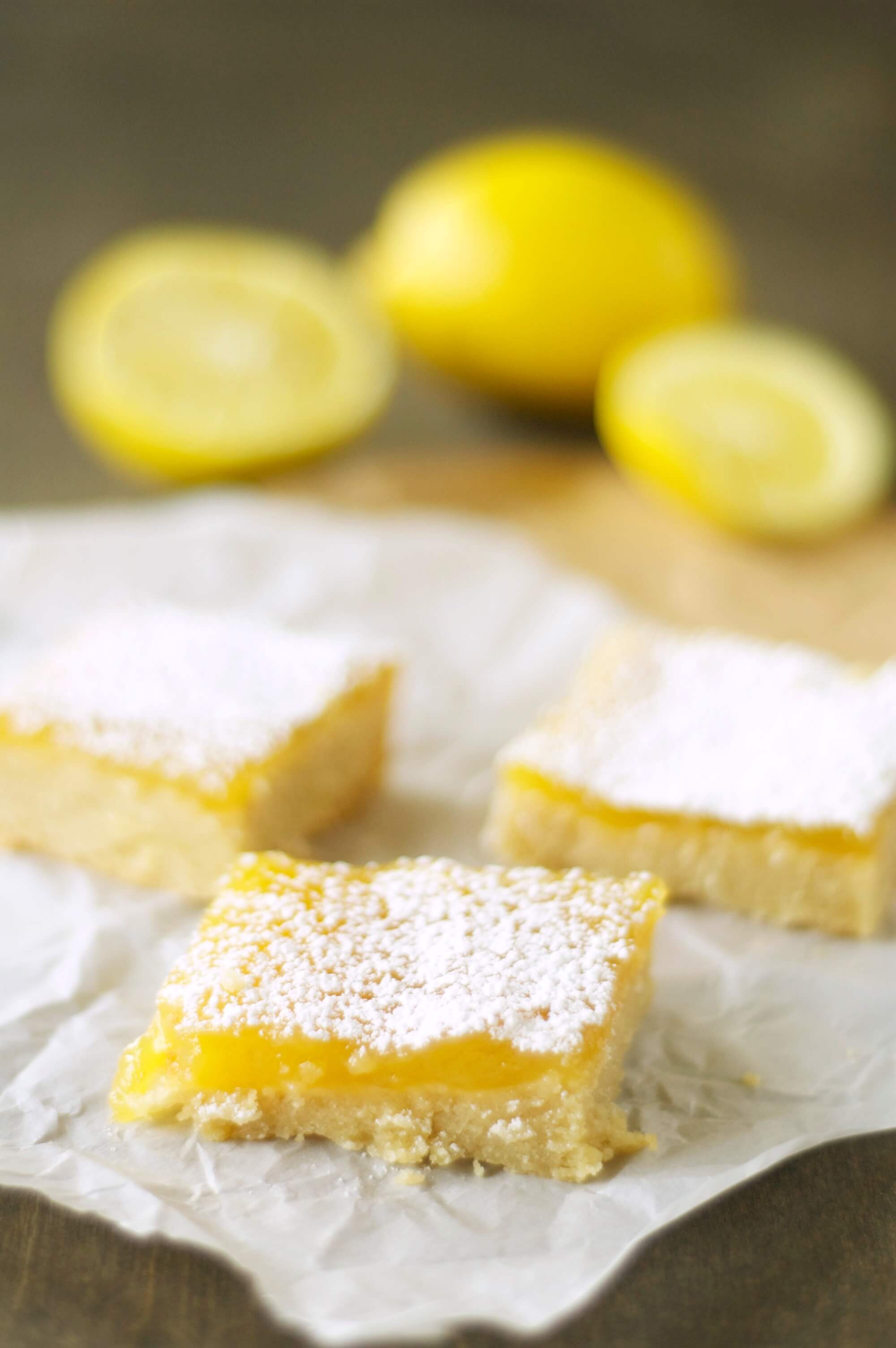 three pieces of lemon cookie bars with two halves and one whole lemon in background
