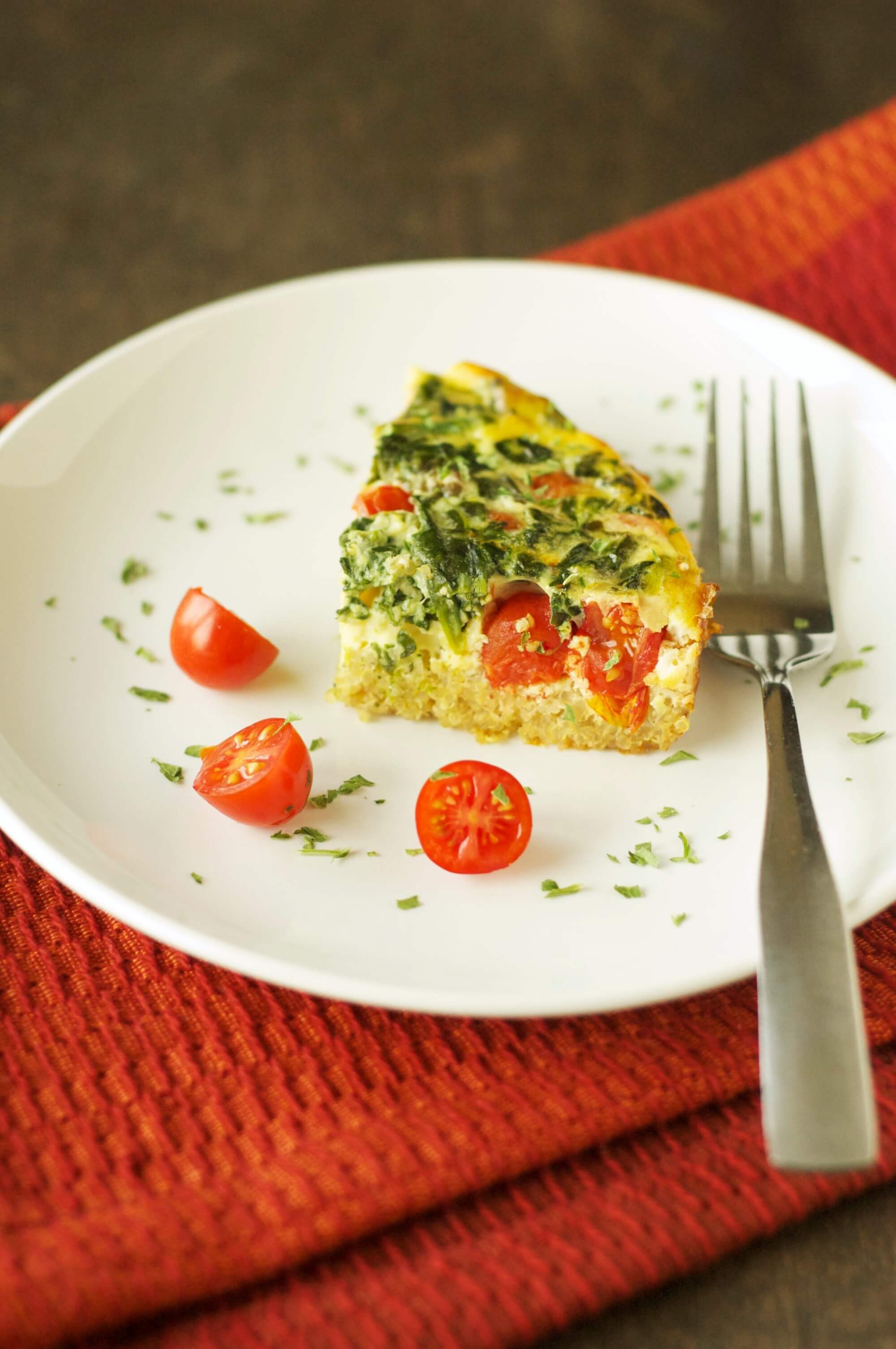 white plate with one piece of breakfast casserole with 3 slices of tomato and fork on plate
