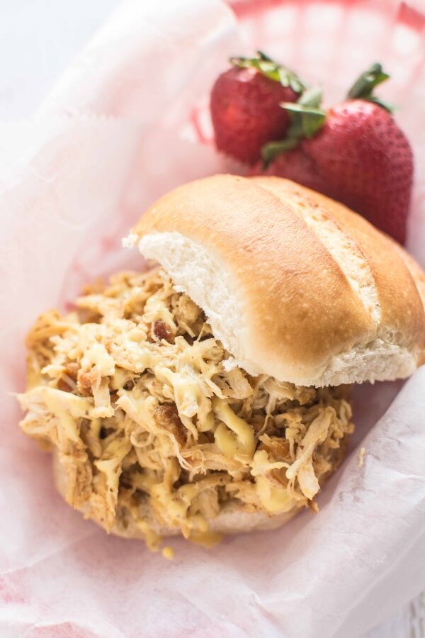 pulled chicken sandwich on bun in parchment lined basket with strawberries in background