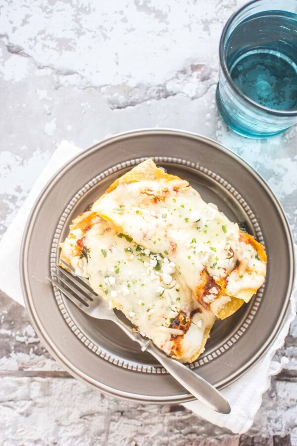 two mushroom enchiladas on gold plate with knife and blue water glass in background