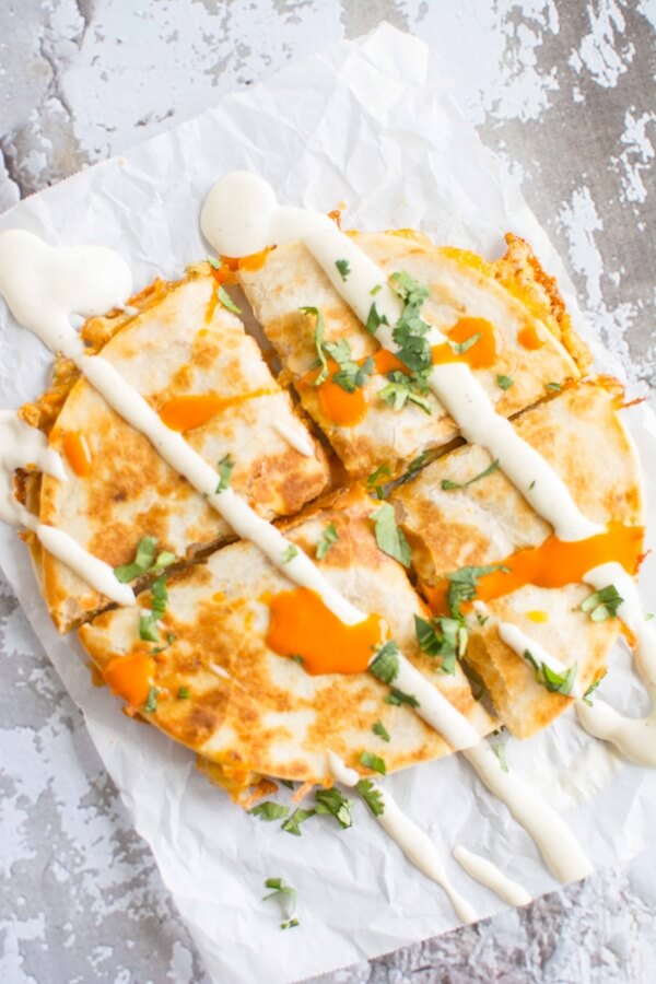 cut up quesadilla on parchment paper drizzled with buffalo sauce and ranch dressing