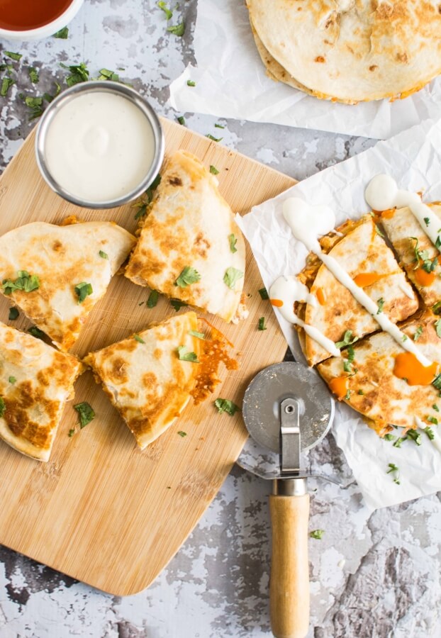 quesadilla on parchment paper, 4 pieces of quesadilla on cutting board with 2 small bowls of ranch dressing and red sauce 