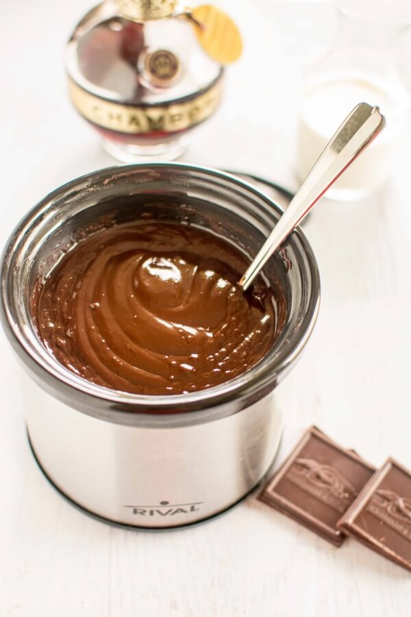chocolate dip in small stainless steel slow cooker with spoon, surrounded by ingredients