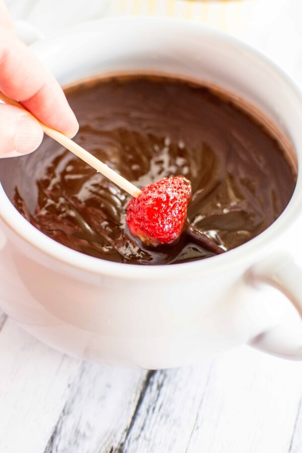 white bowl of chocolate dip; toothpick with strawberry being dipped