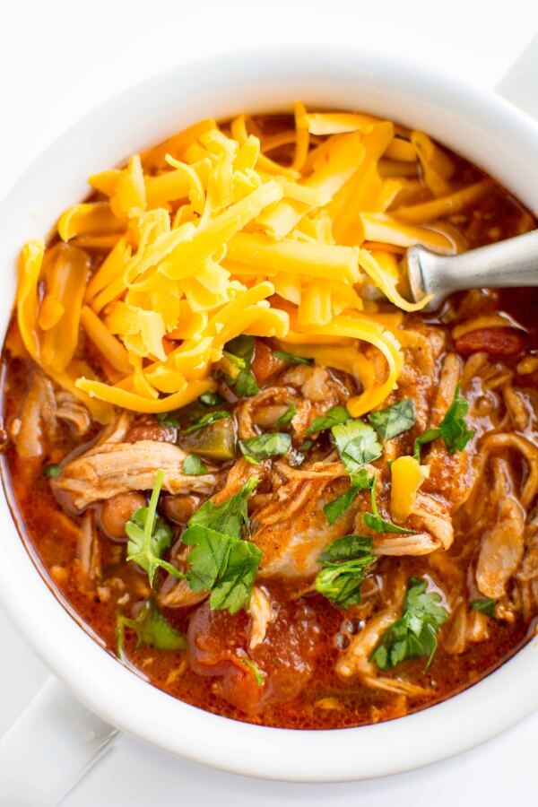 white bowl filled with pulled pork chili, topped with cheese and cilantro with spoon