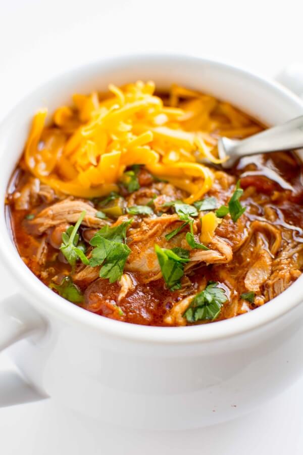 white bowl filled with pulled pork chili, topped with cheese and cilantro with spoon