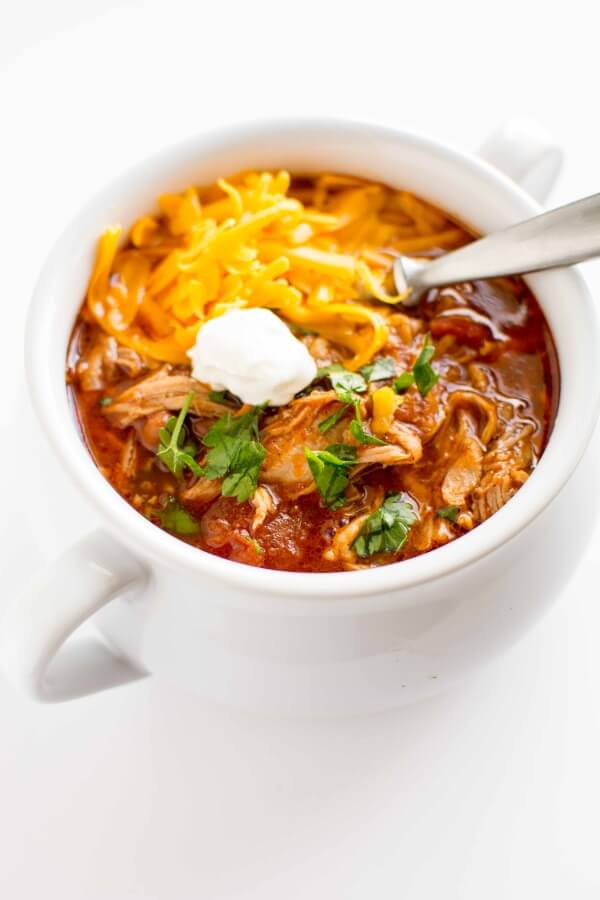 white bowl filled with pulled pork chili, topped with cheese, sour cream and cilantro with spoon