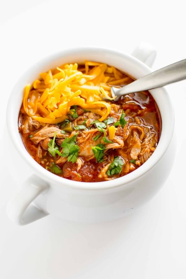 white bowl filled with pulled pork chili, topped with cheese and cilantro with spoon