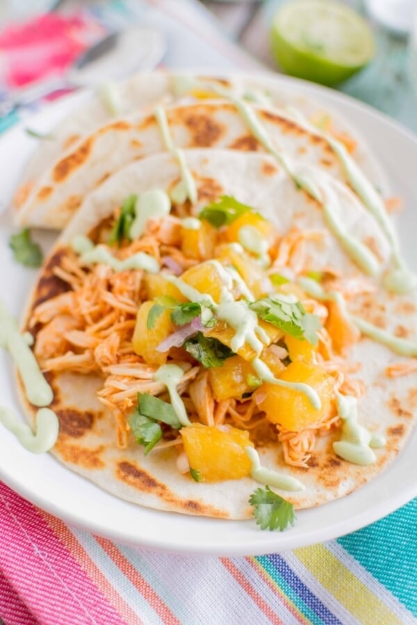 two chicken tacos on white plate drizzled with avocado sauce