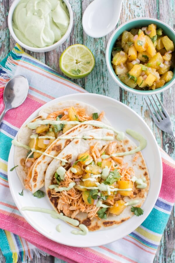 2 chicken tacos on white plate, spoon on side; white bowl with avocado sauce, green bowl with salsa, lime in background