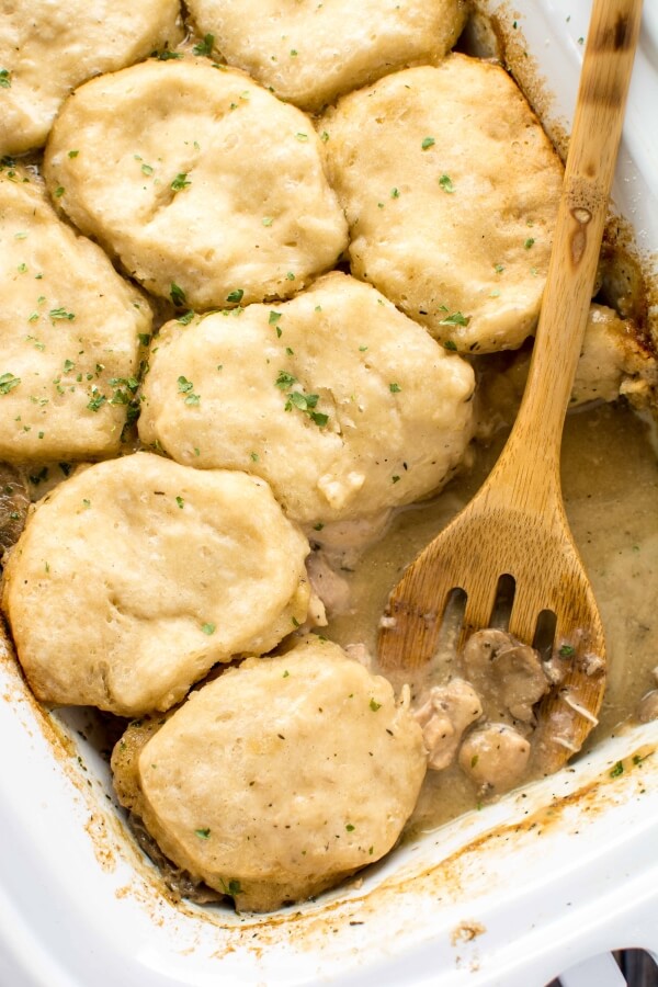 white slow cooker filled with Chicken Gravy and Biscuits with wooden spoon