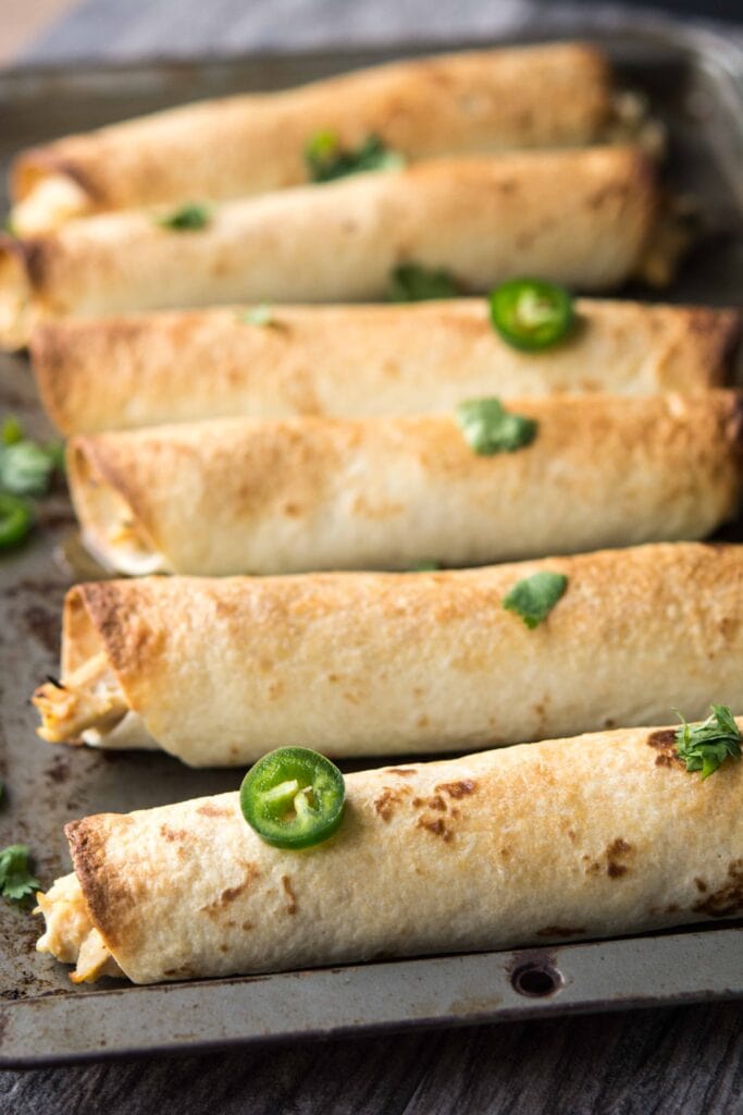 Slow Cooker Jalapeno Popper Chicken Flautas on a baking sheet before sour cream is added on top.