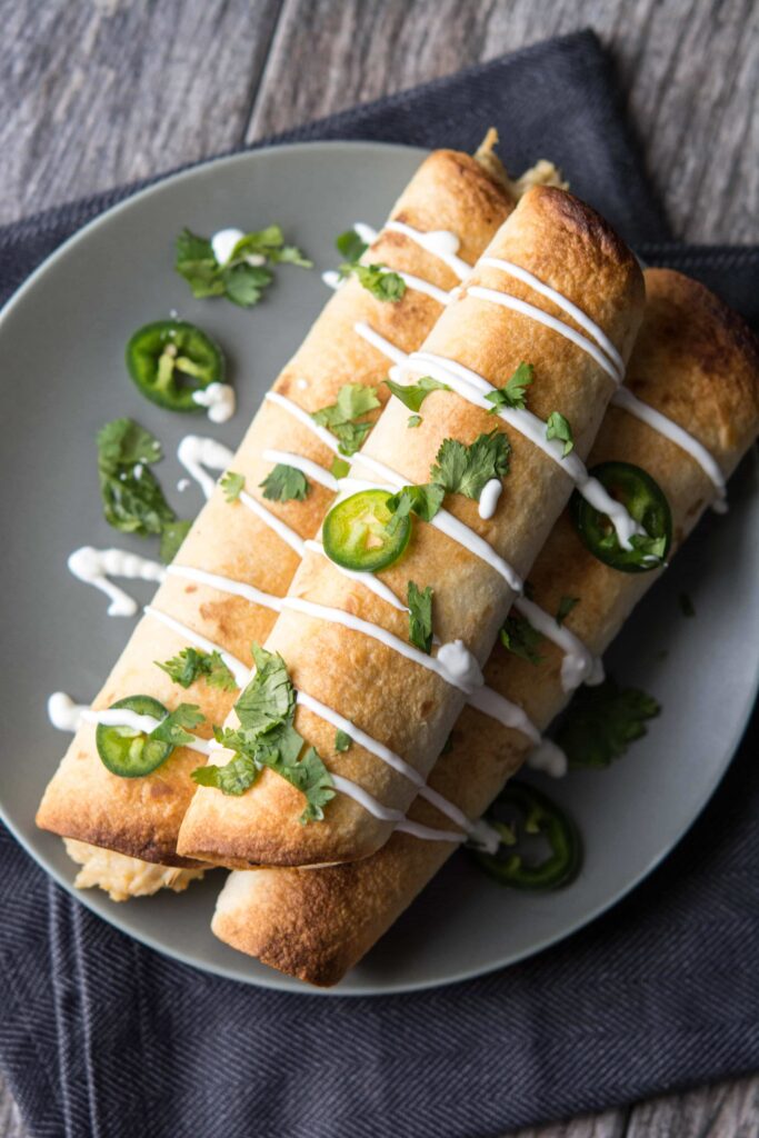 Overhead view of Slow Cooker Jalapeno Popper Chicken Enchiladas with sour cream drizzle and cilantro