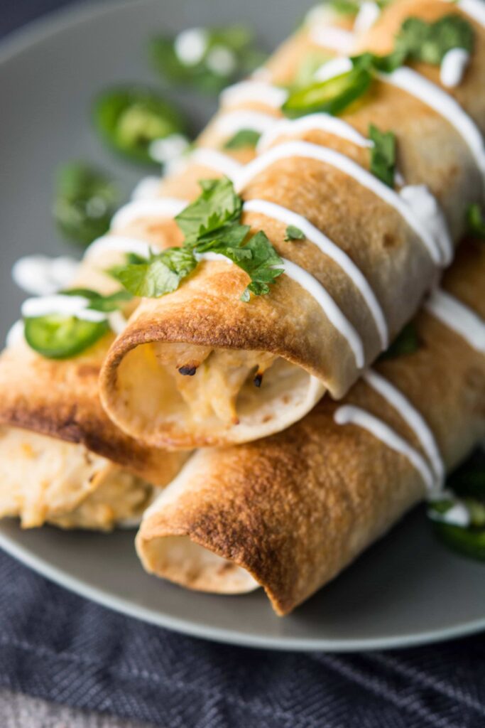 Slow Cooker Jalapeno Popper Chicken Enchiladas on a grey plate with sour cream and cilantro.