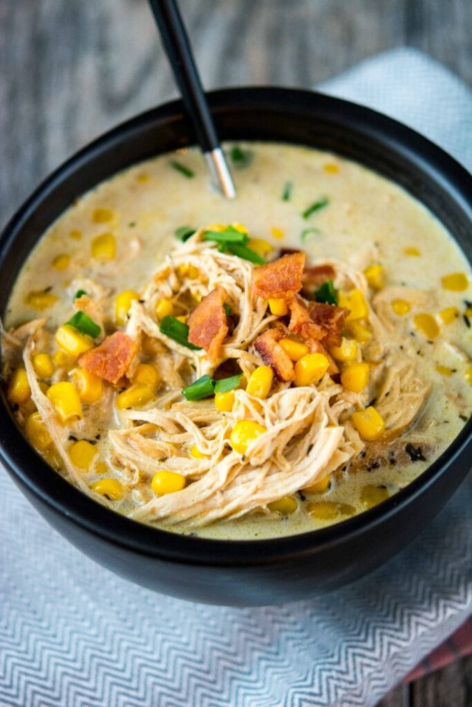 Slow Cooker Chicken Corn Chowder in a black bowl with a black spoon topped with bacon.
