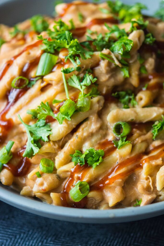 closeup of bbq chicken pasta in blue bowl with herb garnishing