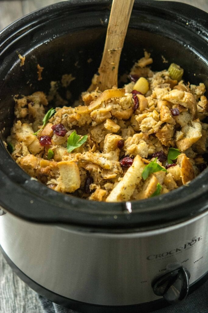 Slow Cooker Stuffing with Caramelized Apple and dried cranberries in round slow cooker with wooden spoon