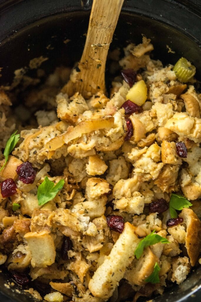 Slow Cooker Stuffing with Caramelized Apple and dried cranberries in round slow cooker with wooden spoon