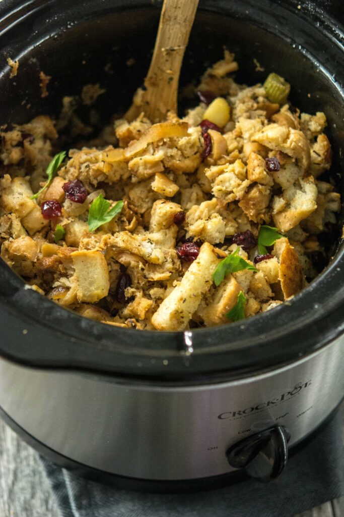 Slow Cooker Stuffing with Caramelized Apple and dried cranberries in round slow cooker with wooden spoon