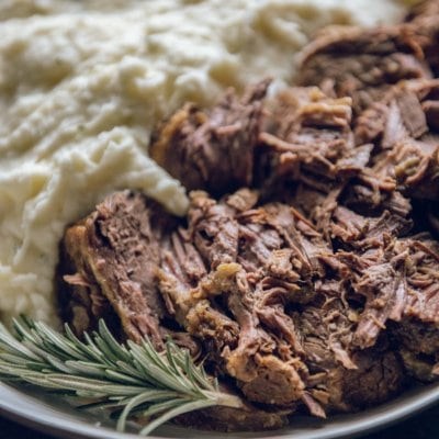 Slow Cooker Roast Beef with mashed potatoes in a white bowl with a sprig of rosemary