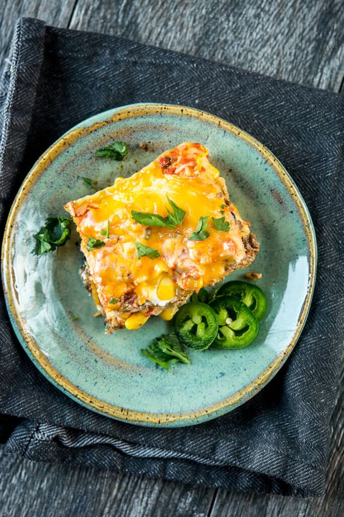 Serving of Slow Cooker Mexican Lasagna garnished with jalapeño on a teal plate resting a a denim napkin.