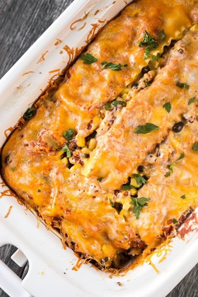 Slow Cooker Mexican Lasagna topped with melted cheese in a white crock.