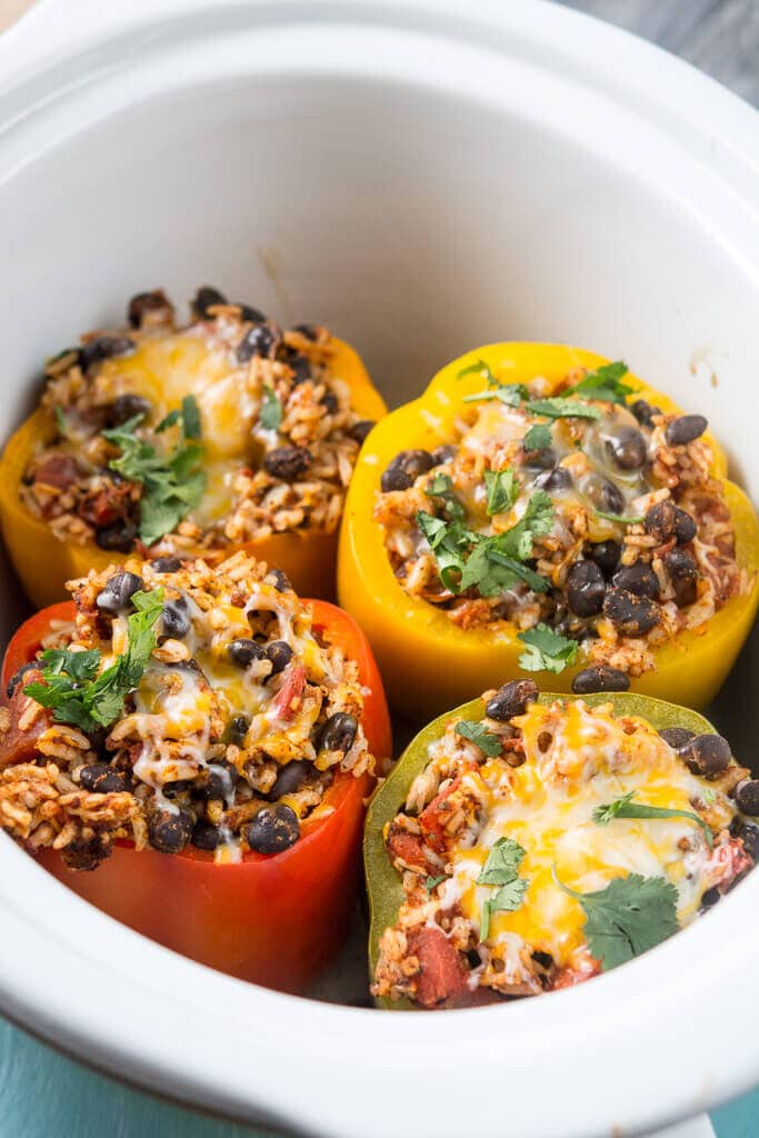 Picture of slow cooker stuffed peppers topped with cilantro in white crock. 