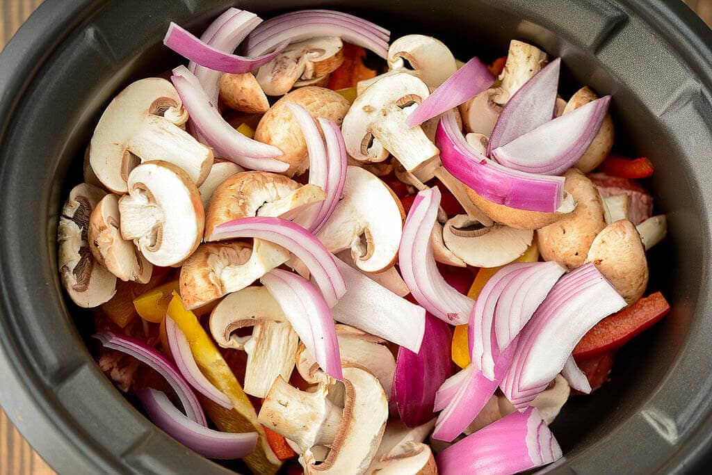 Onions and mushrooms layered over skirt steak - Slow Cooker Steak Fajitas