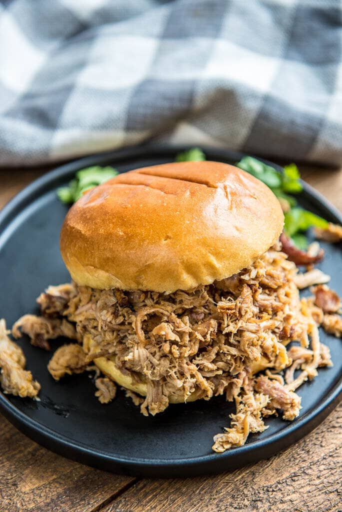 pulled pork sandwich on a black plate with a gray checked napkin in the background