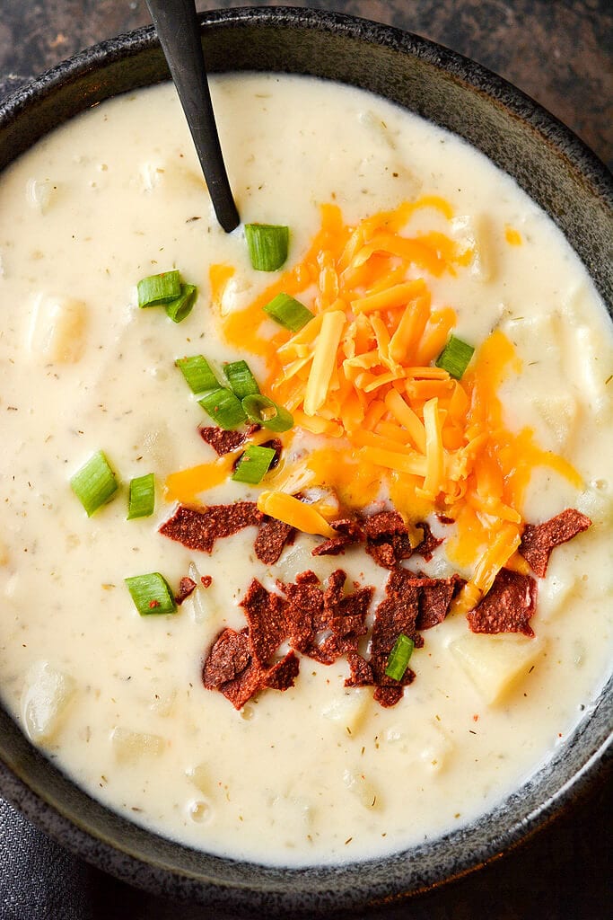 Slow Cooker Loaded Baked Potato Soup topped with bacon and cheese in a black bowl with a black soon.
