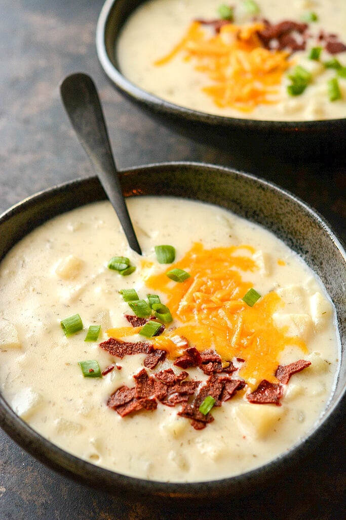 Close up shot of two servings ofSlow Cooker Loaded Baked Potato Soup, topped with bacon and cheese in black bowls.