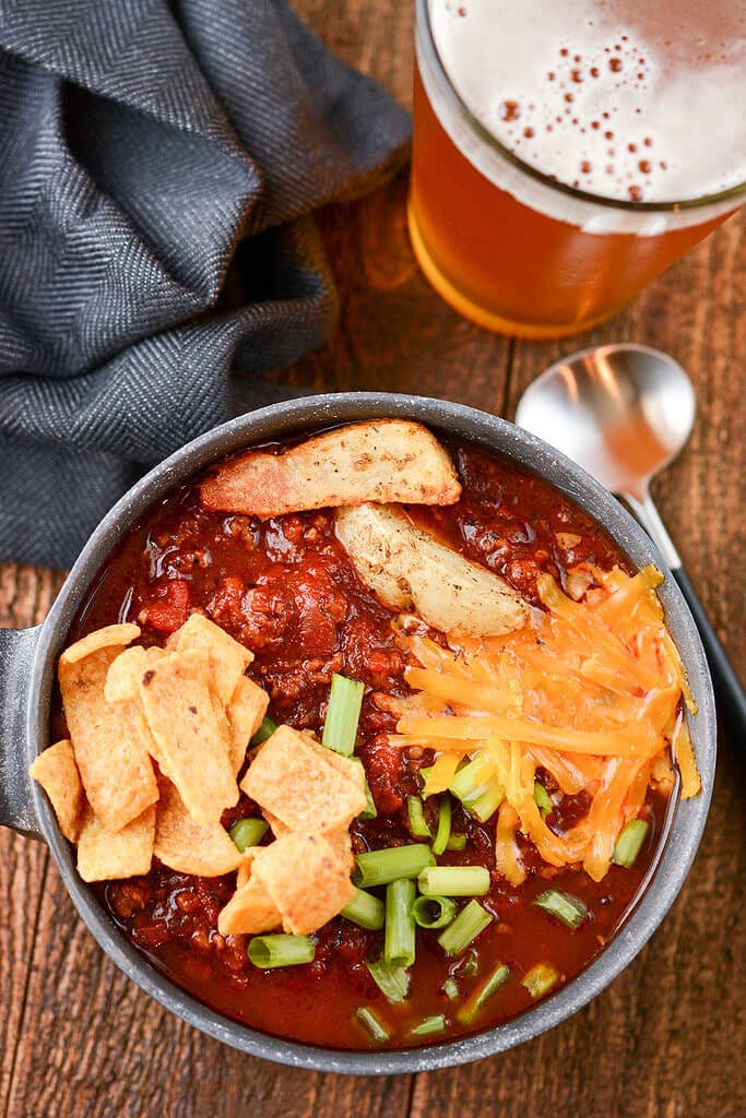 Slow Cooker Tailgate Chili in a bowl with chili topping and a beer