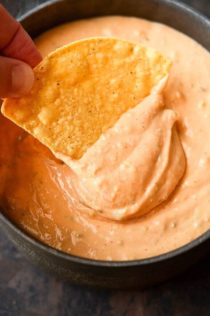 Dipping chip in Slow Cooker Spicy Queso in a black bowl.