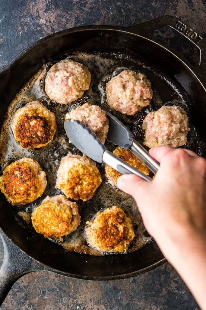 browning meatballs in a skillet, turning with tongs