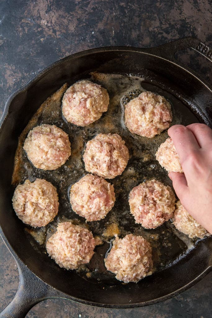 adding meatballs to a cast iron skillet to brown
