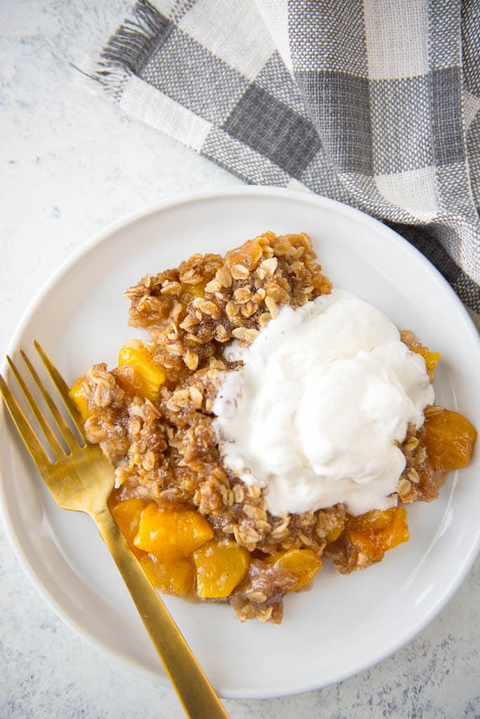 Looking for a delicious treat to use all those farmer's market fresh peaches? Slow Cooker Peach Cobbler with Fresh Peaches and the most delicious Yogurt Whipped Cream is the perfect summer dessert!