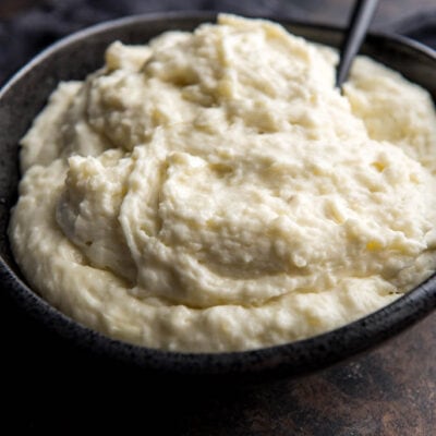 Side view of fluffy pressure cooker instant pot mashed potatoes in a black serving bowl on a black countertop with a serving spoon