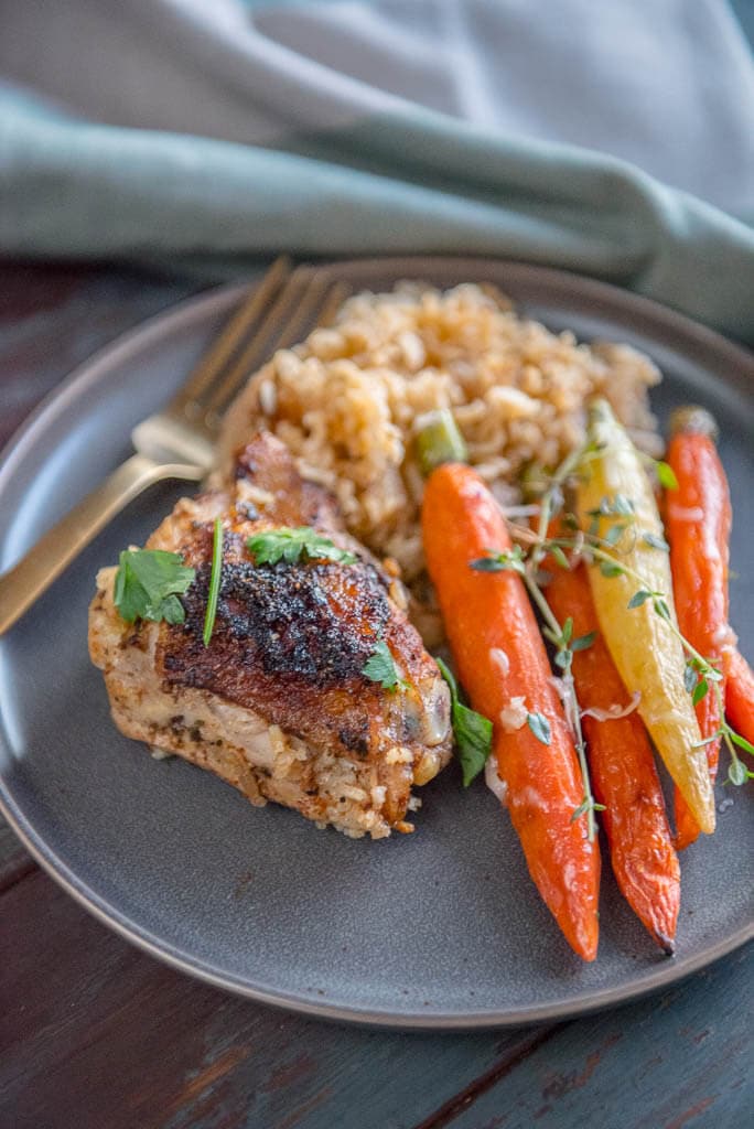 Slow Cooker Baked Chicken Thighs with rice on gray plate with gray napkin and carrots