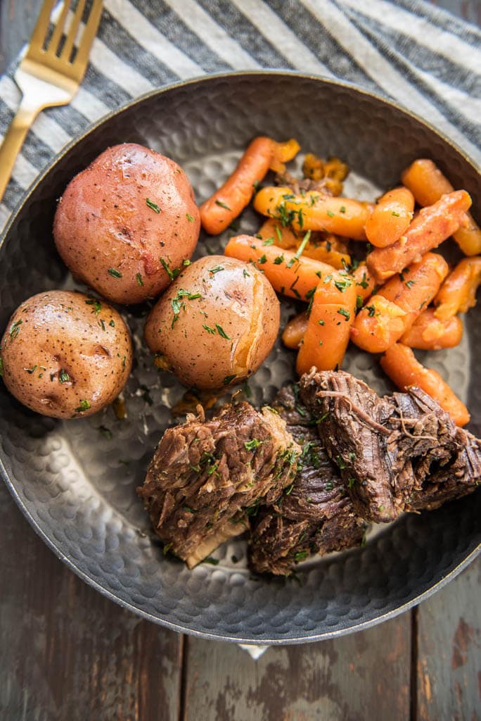 Pressure Cooker Pot Roast on a metal plate served with carrots and potatoes on a table with a gray and white napkin and gold fork