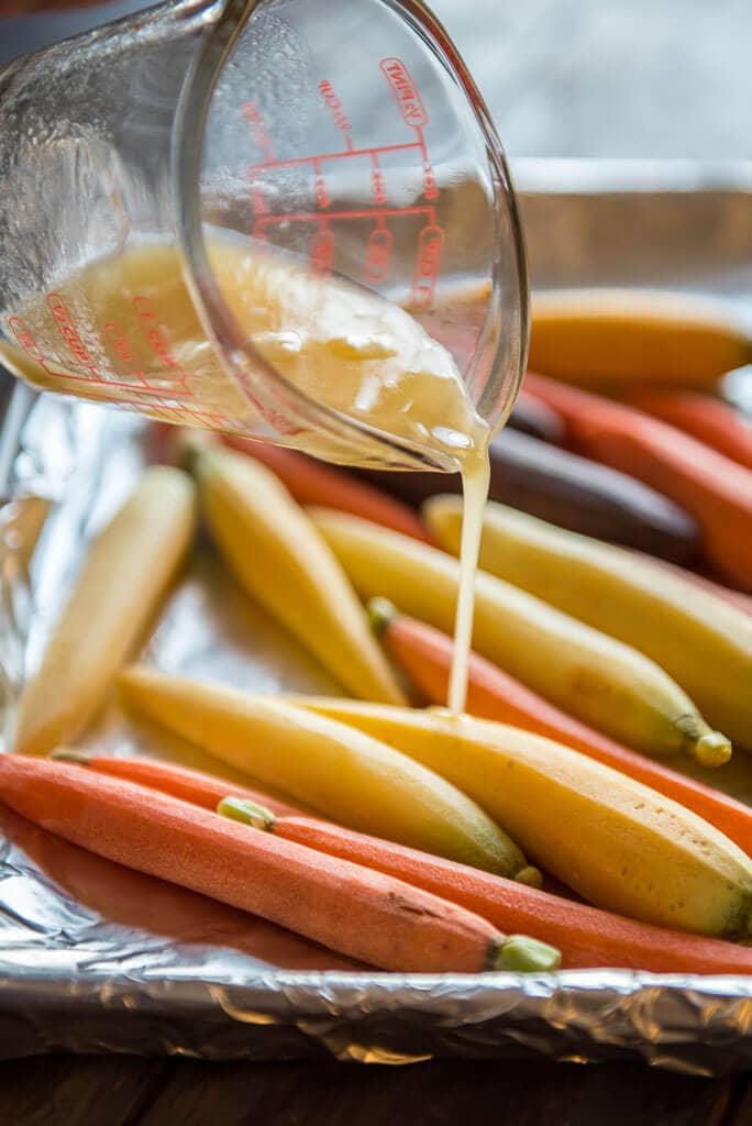 honey butter sauce being drizzled on carrots on baking sheet