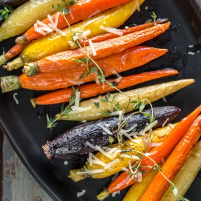 Multi-color oven roasted carrots on black serving platter topped with fresh thyme