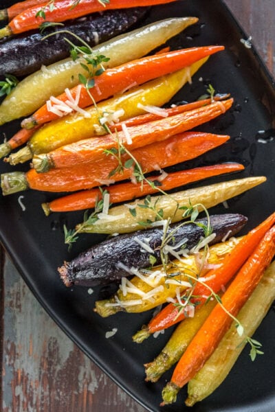 Multi-color oven roasted carrots on black serving platter topped with fresh thyme