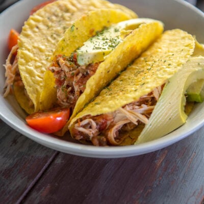 Tacos stuffed with Slow Cooker Salsa Chicken on a gray plate topped with tomato and avocado