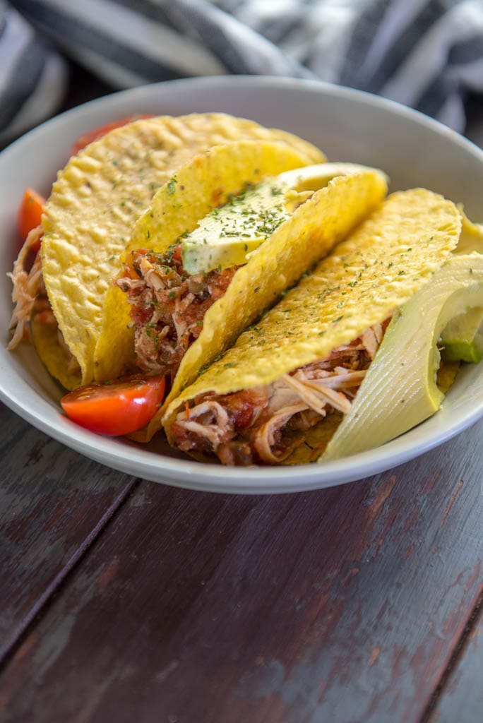 Tacos stuffed with Slow Cooker Salsa Chicken on a gray plate topped with tomato and avocado